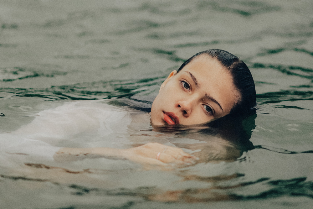 Editorial image of woman in white linen floating in water