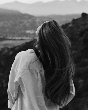 Monochrome image of woman standing on the hills looking up at the sky