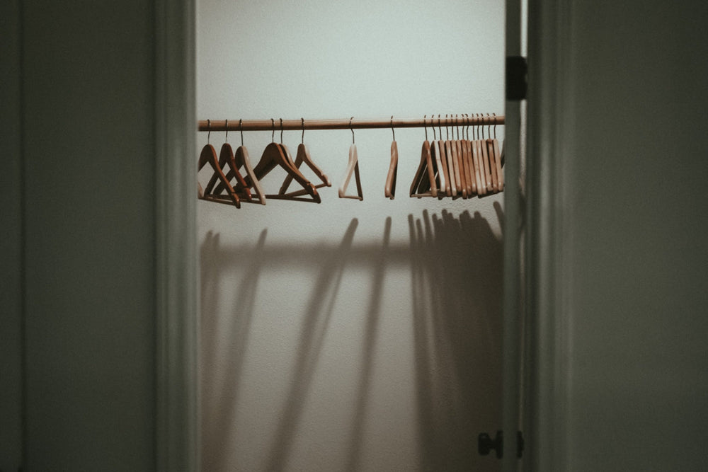 An empty closet with hangers left on the rail with editorial shadows and lighting.