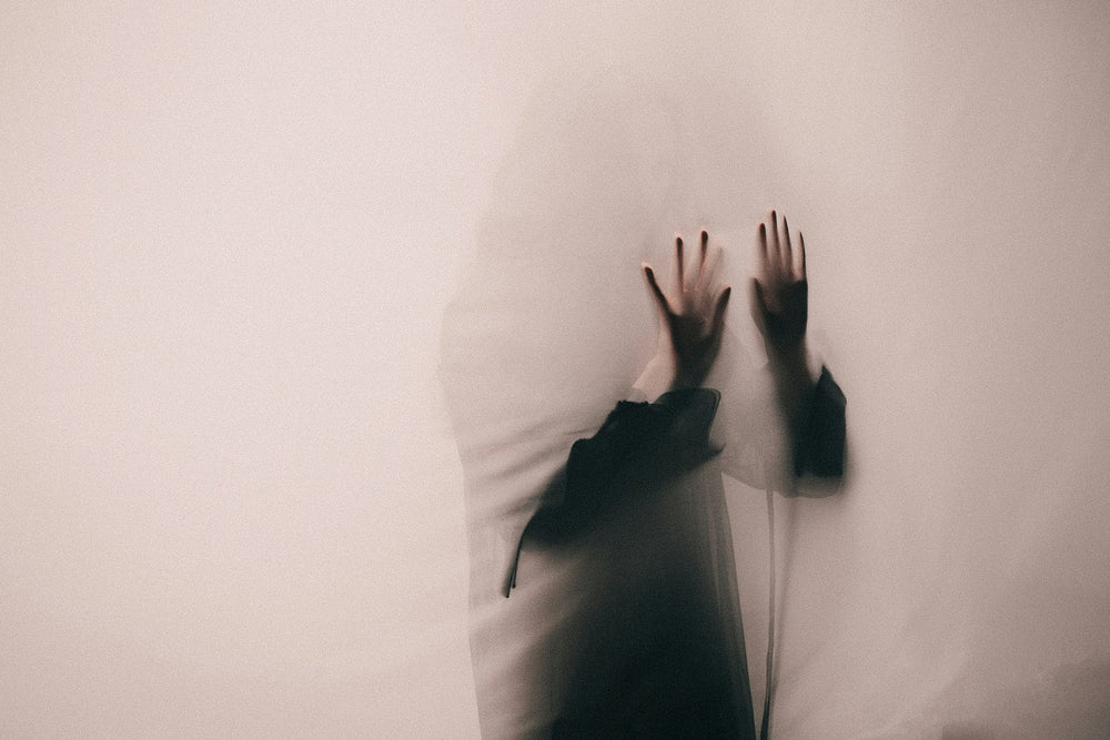 A woman behind a thin veil with her hand pressed against it as a shadowy figure.