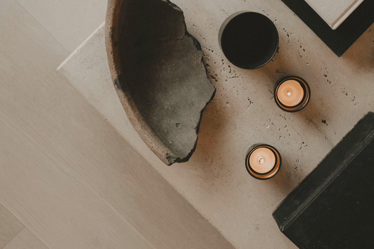 Editorial image of two burning candles and a broken stone plate on a neutral cement surarce.