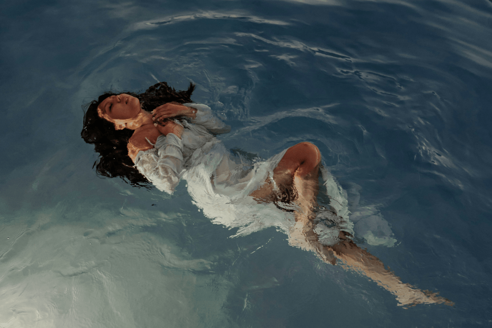 Editorial image of woman in white linen floating in water