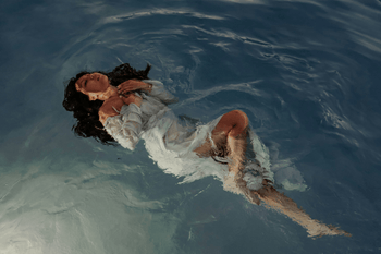 Editorial image of woman in white linen floating in water