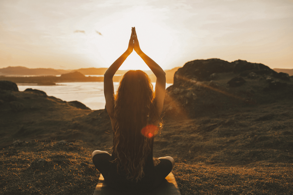 A woman doing yoga with a sunset in the background.