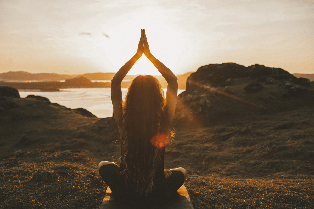 A woman doing yoga with a sunset in the background.
