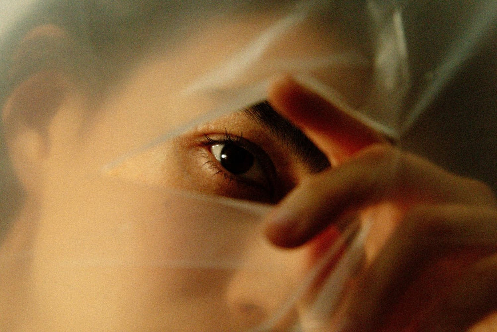 Editorial image of woman peeking through a small hole on a sheer thin fabric.