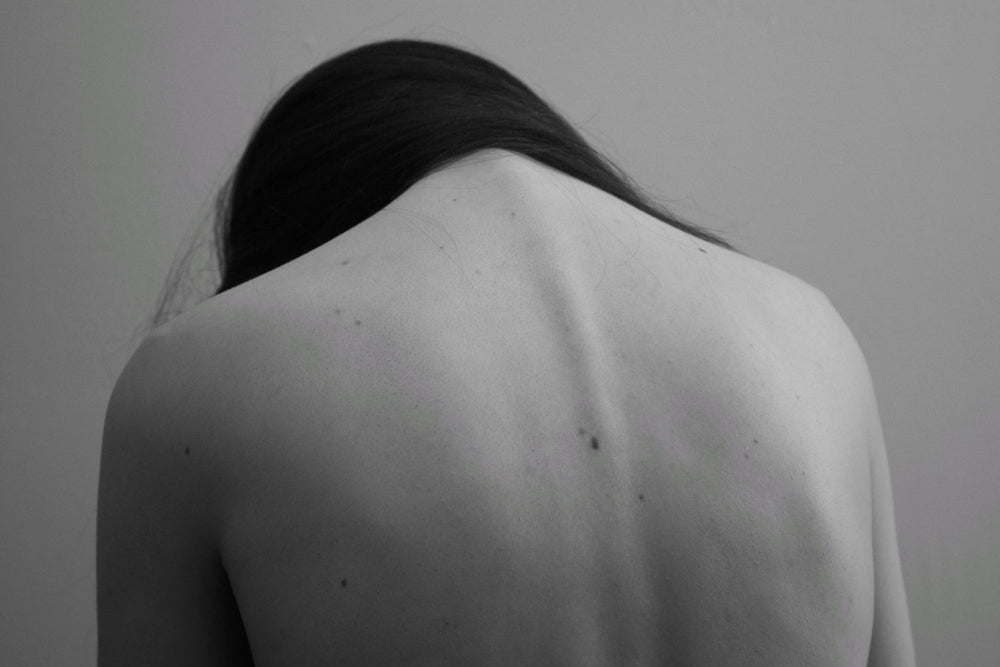 Monochrome image of woman's bare back with her head down.