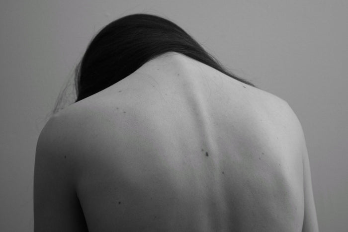 Monochrome image of woman's bare back with her head down.