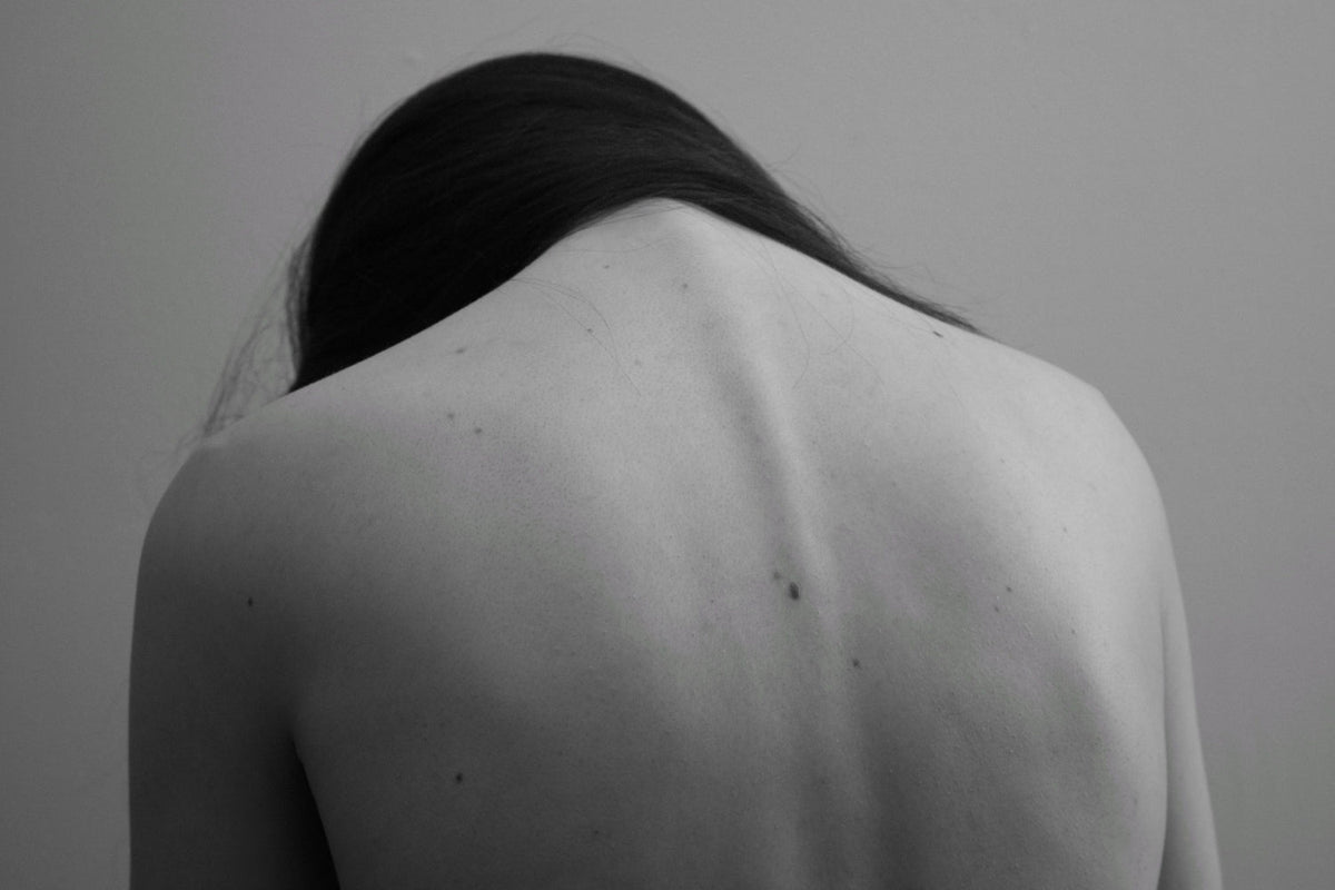Monochrome image of woman's bare back with her head down.