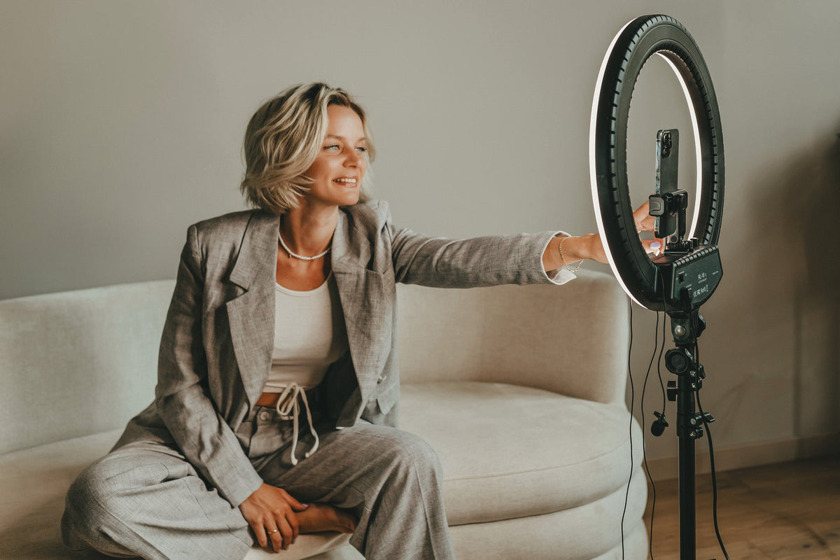 Woman on on a beige sofa with a ring light for content creation.