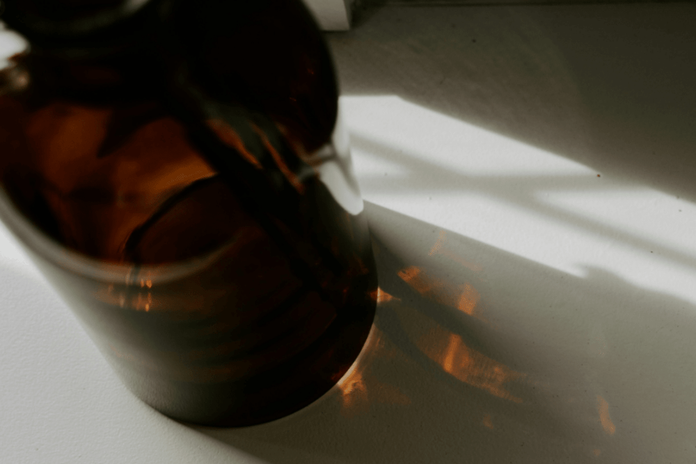 Editorial image of amber fragrance bottle with amber shadows on neutral background.