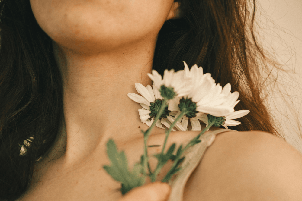A close up image of white lowers against a woman's shoulder on neutral background.