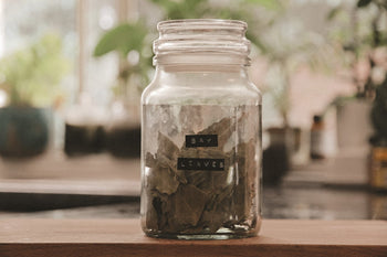 Jar of bay leaves on a open kitchen counter with jars and open windows in the background