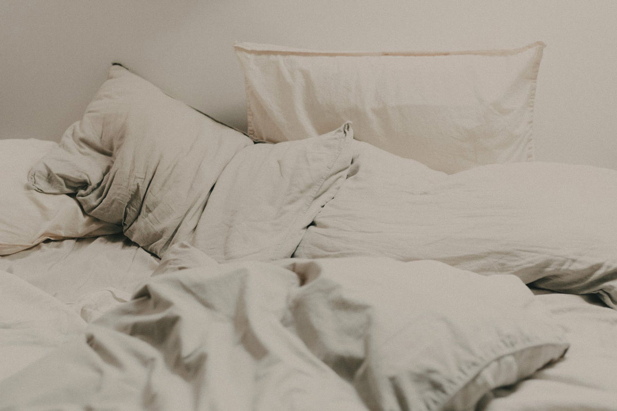 Editorial image of an unmade bed with neutral light beige linen sheets and pillows.
