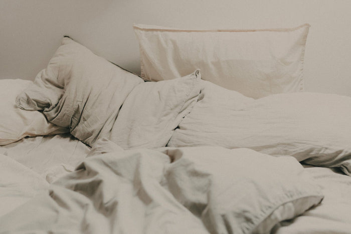 Editorial image of an unmade bed with neutral light beige linen sheets and pillows.