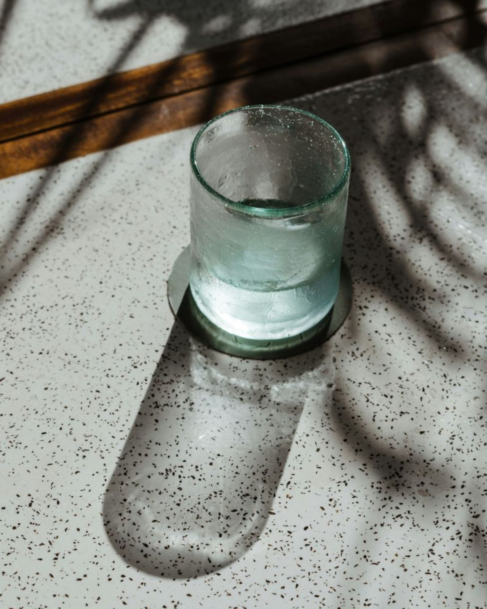 A glass cup being filled with water on a neutral table with  greenery in the background.