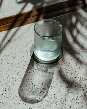 A glass cup being filled with water on a neutral table with  greenery in the background.
