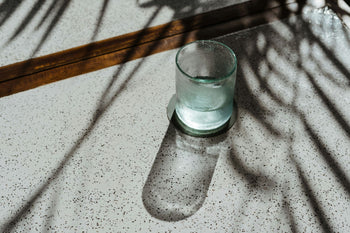 A glass cup being filled with water on a neutral table with  greenery in the background.
