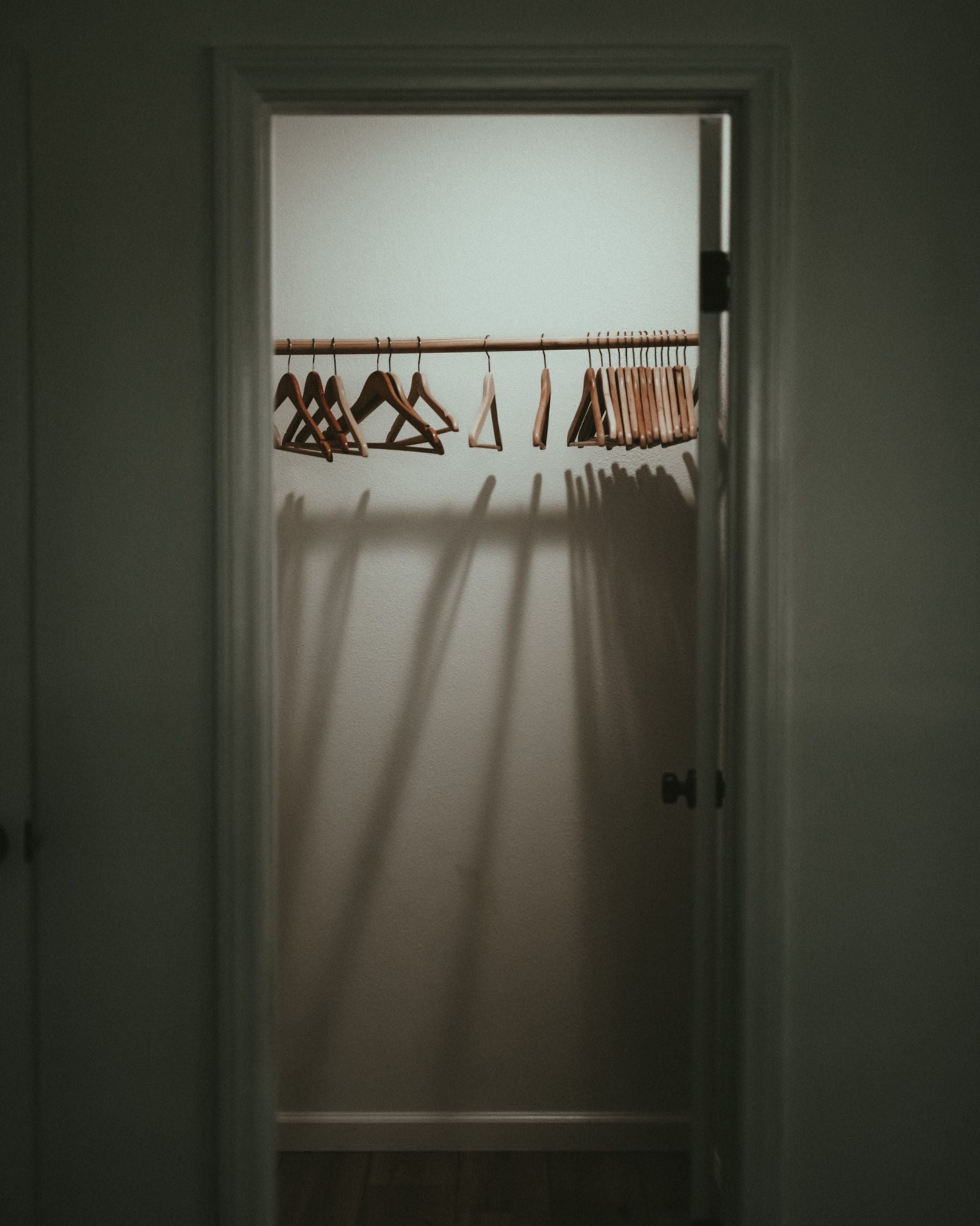 An empty closet with hangers left on the rail with editorial shadows and lighting.