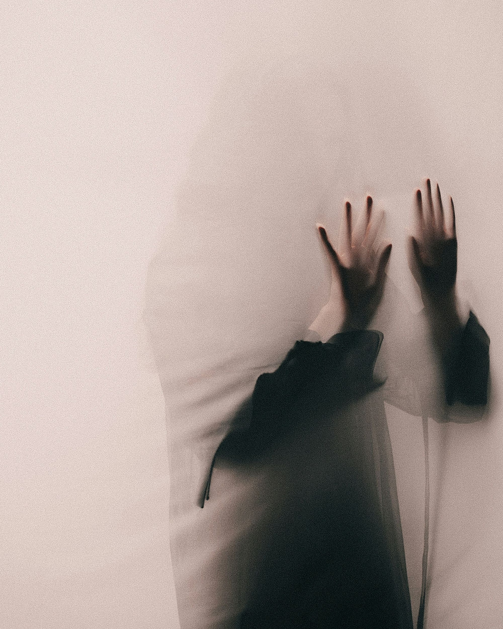 A woman behind a thin veil with her hand pressed against it as a shadowy figure.