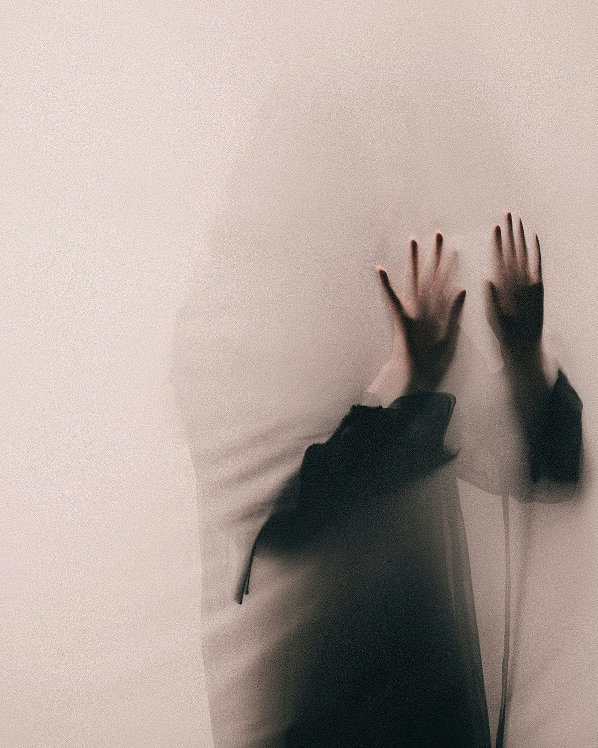 A woman behind a thin veil with her hand pressed against it as a shadowy figure.