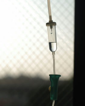 A glass cup being filled with water on a neutral table with  greenery in the background.