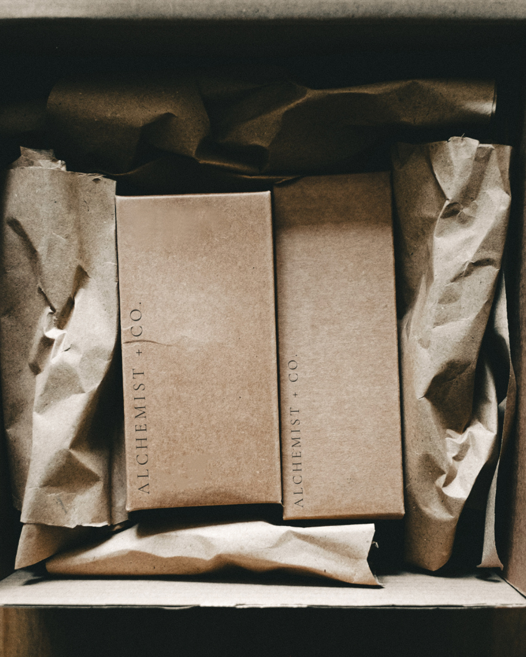 Two brown packages with 'Alchemist + Co.' branding inside a box.