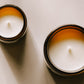 Alchemist + Co. Bare Collection candles in amber glass vessels with warm directional light and soft shadows.