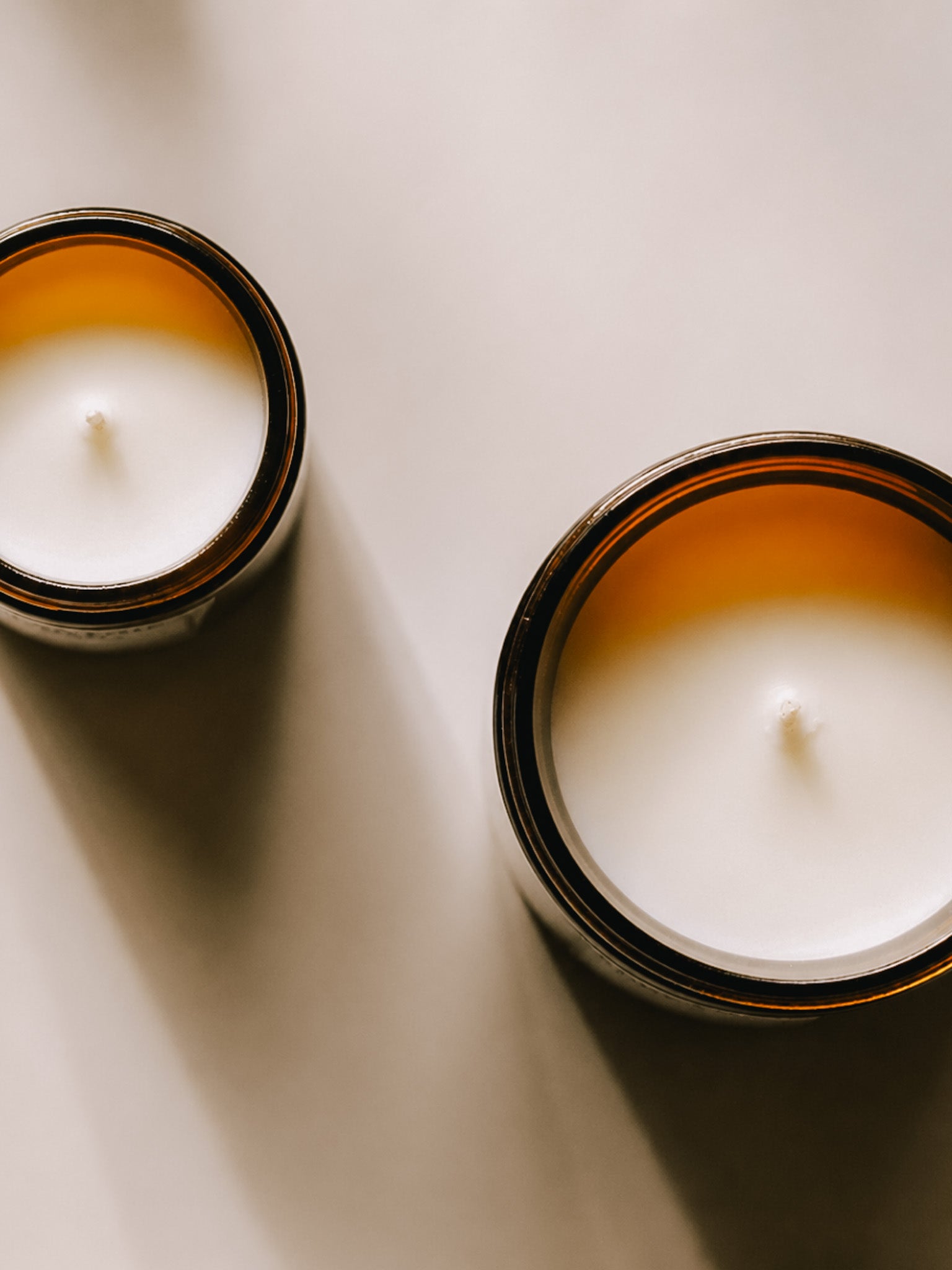 Alchemist + Co. Bare Collection candles in amber glass vessels with warm directional light and soft shadows.