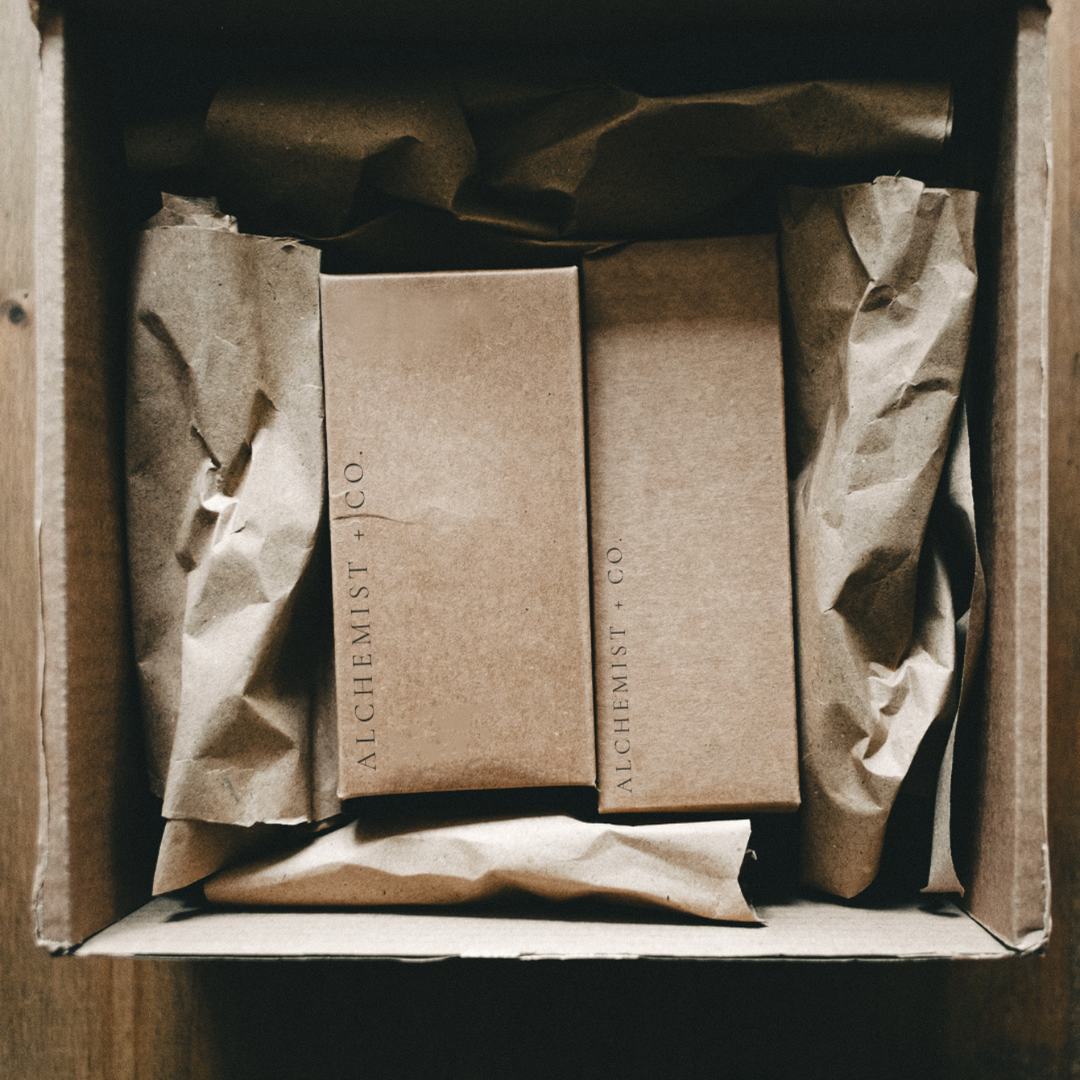 Two brown boxes with 'Alchemist + Co.' branding inside a cardboard box