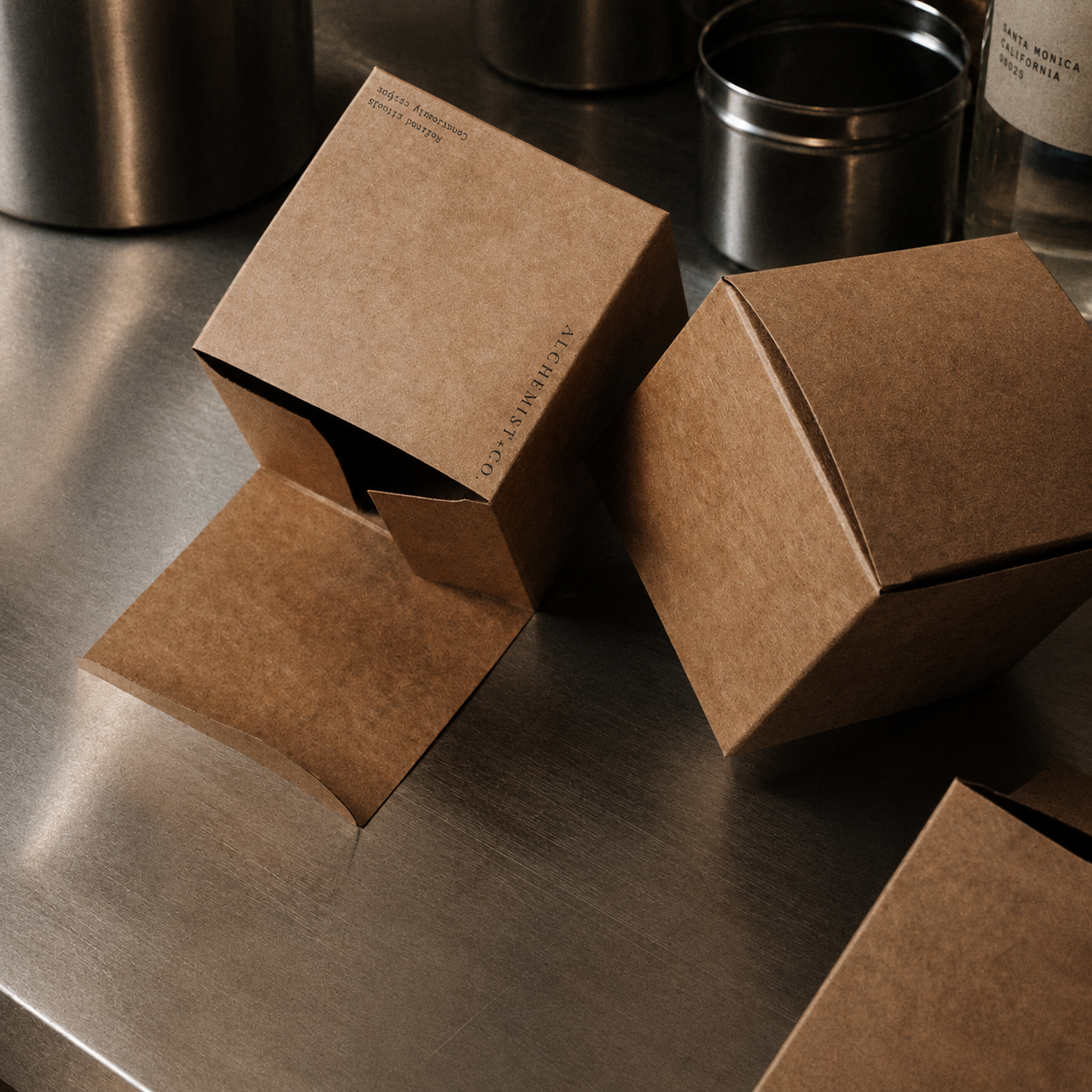 Brown paper boxes branded Alchemist + Co. on a metallic surface