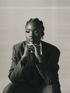 Aquarius woman in a suit sitting in a pensive position against a neutral background.