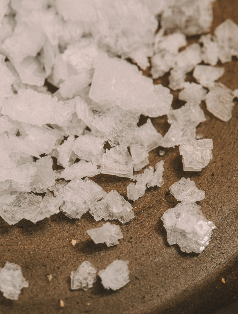 Flaky sea salt crystals scattered across a dark stoneware surface, the hero note of the Aquarius candle