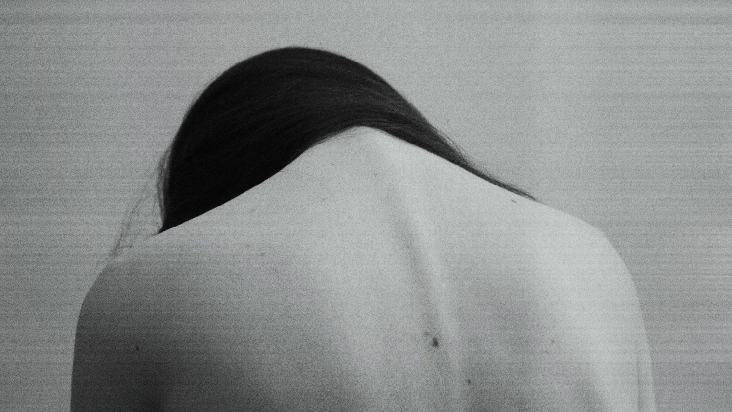 Libra woman with long hair from behind against a plain background in a slumped defeated position.