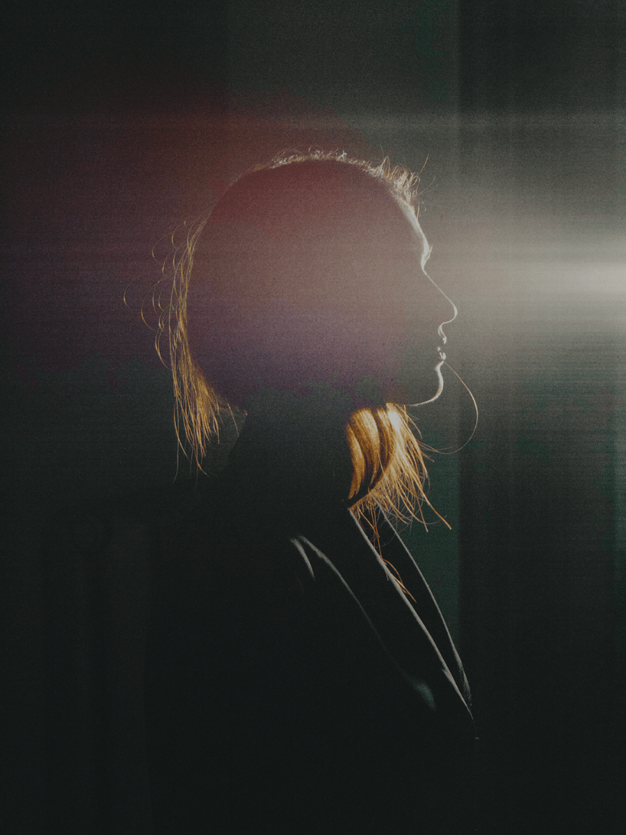 An Aries woman sitting on a chair in a dark room with soft light on her face.