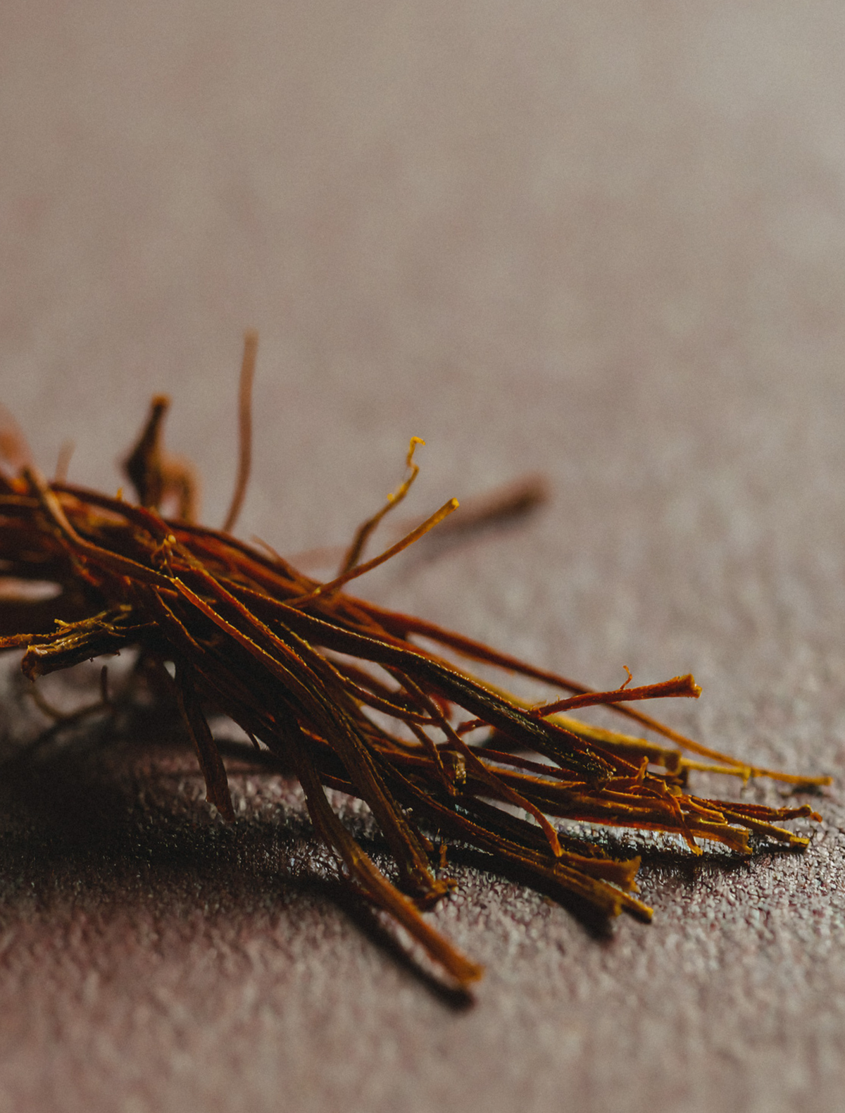 A loose bundle of dried saffron threads on a dark textured surface, the hero note of the Aries candle