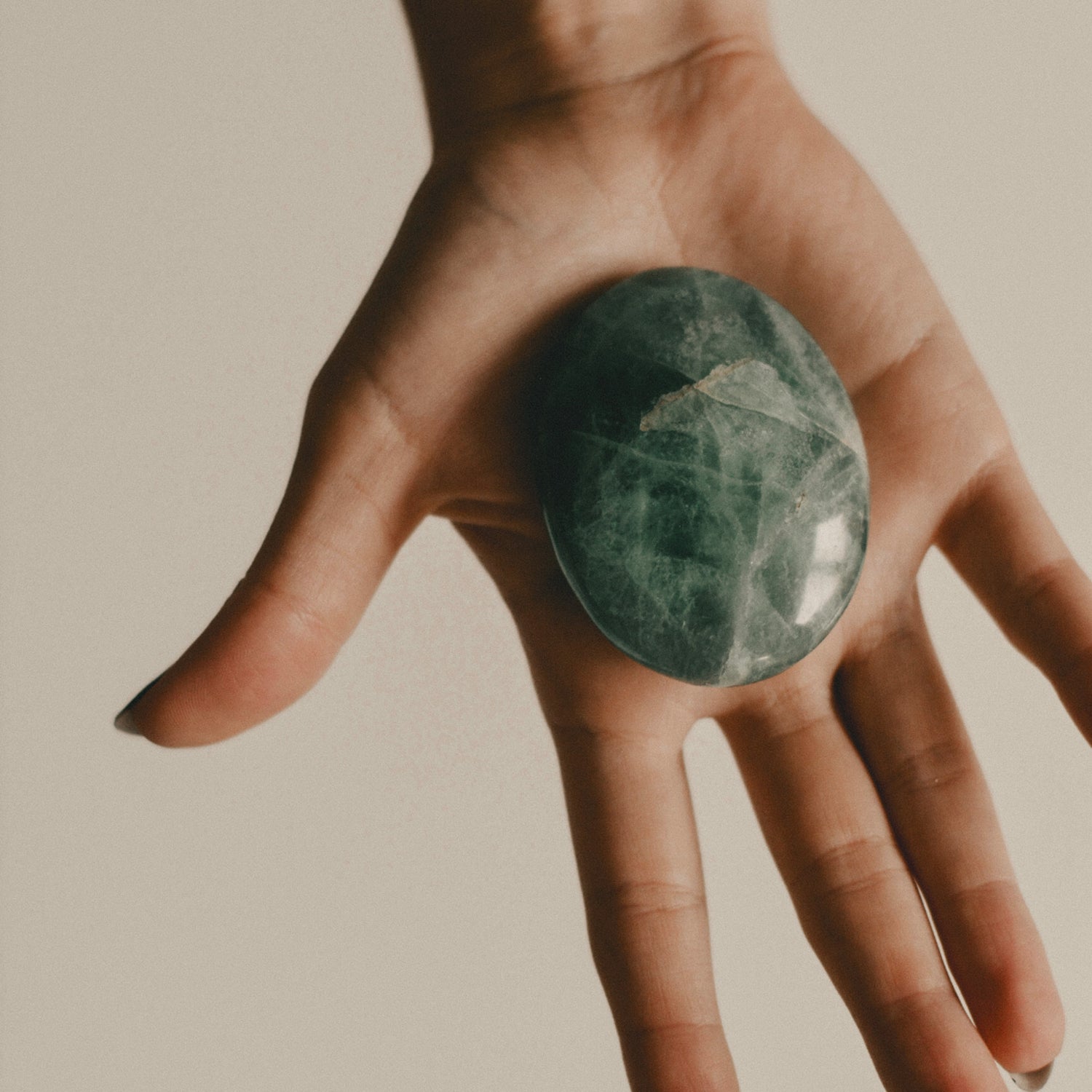 Hand holding a green aventurine tone against a neutral background