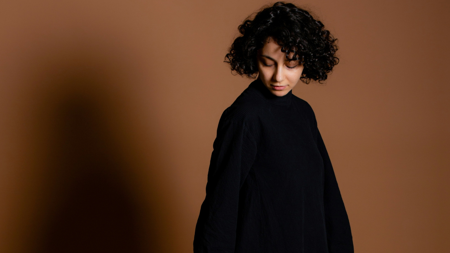 Woman wearing a black hooded garment against a brown background