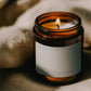 Lit Ayahuasca ritual candle beside textured linen in warm atmospheric light.