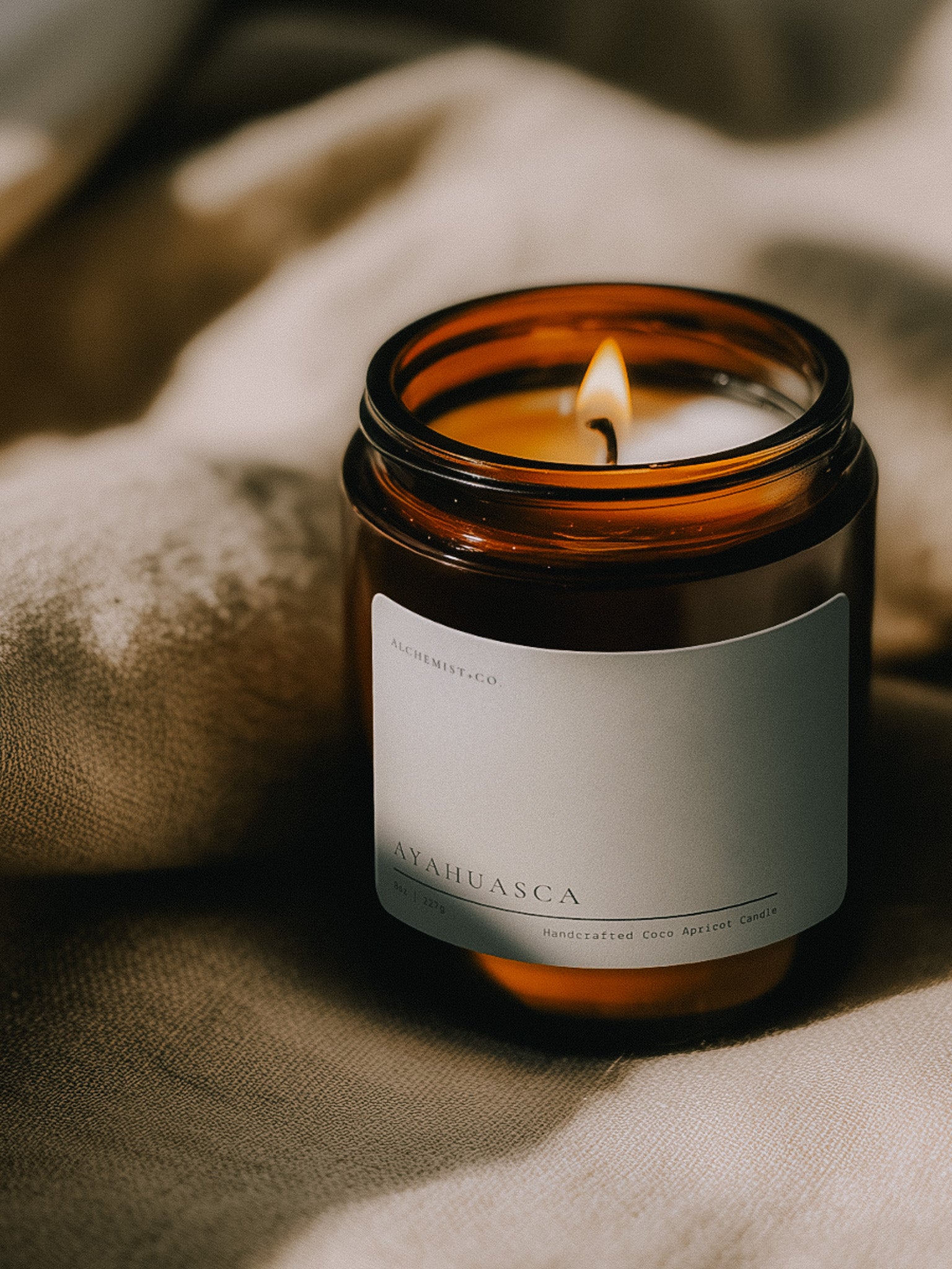 Lit Ayahuasca ritual candle beside textured linen in warm atmospheric light.