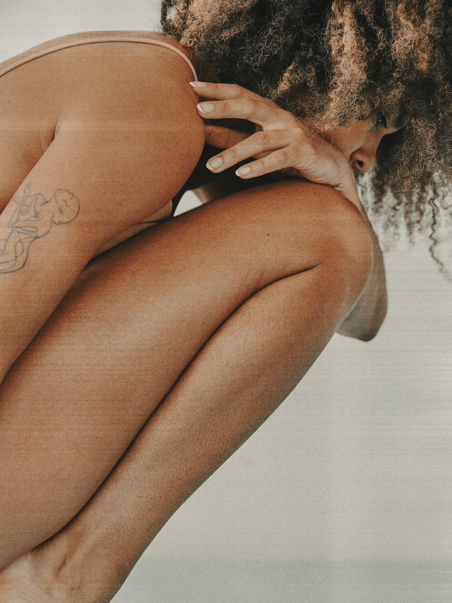 Cancer woman crouched down in defeated position on a neutral background.