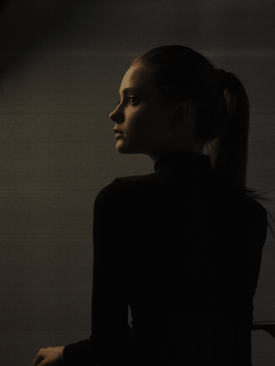 A stoic Capricorn woman in a black turtle neck against dark background with soft light.
