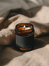 Citrus Palm + Teakwood Bare candle burning beside soft linen in warm atmospheric light.