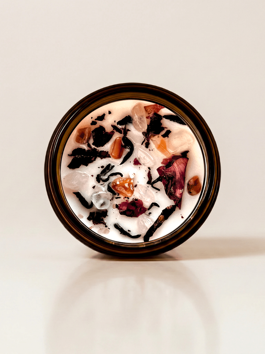 Dark Feminine ritual candle with carnelian, rose quartz, quartz, and botanical details viewed from above. 