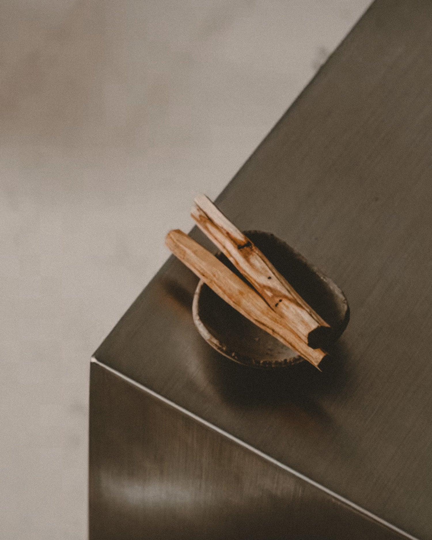 Two Palo Santo sticks in a small bowl on a metallic surface.