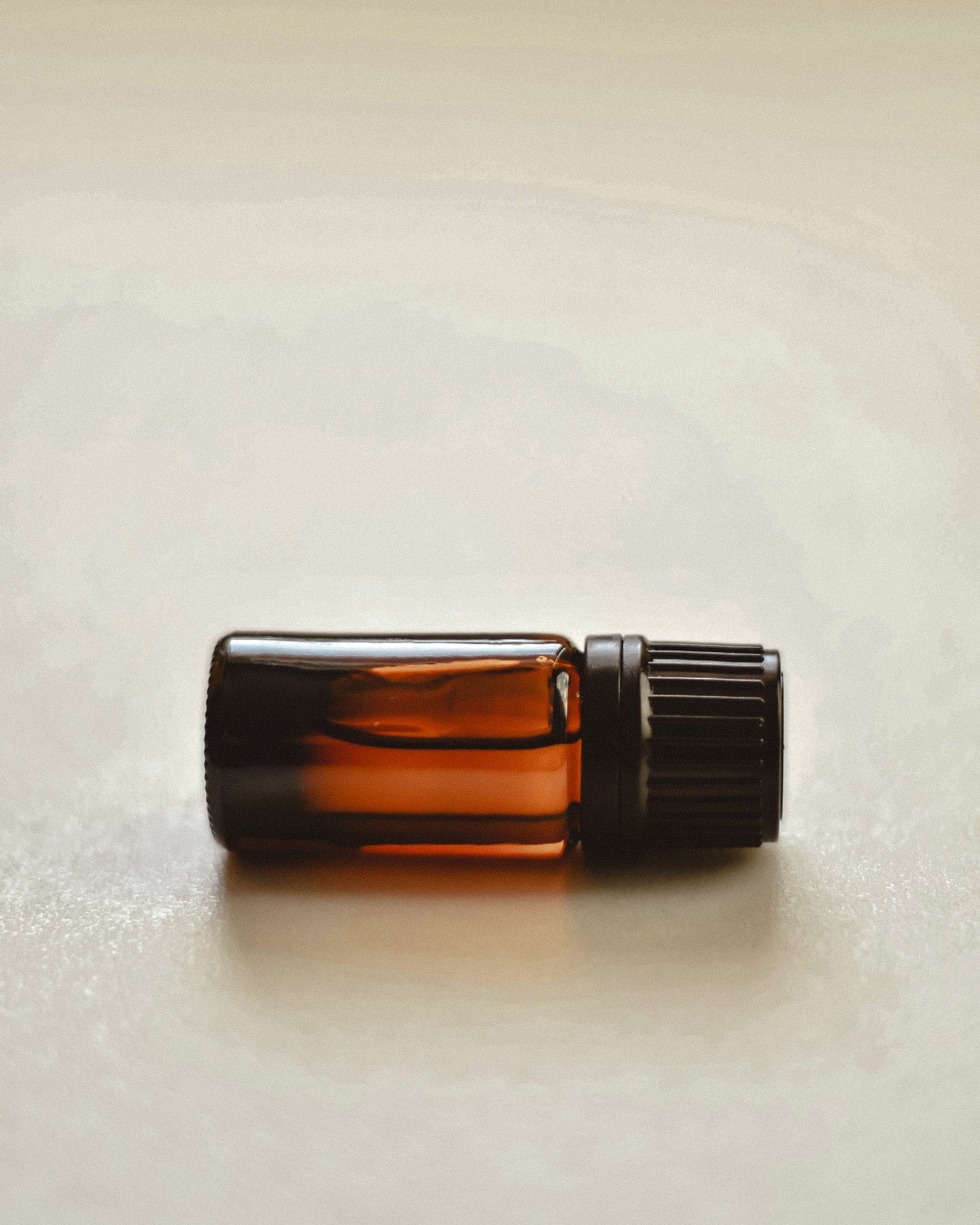 Small amber glass bottle with a black cap on a light beige background.