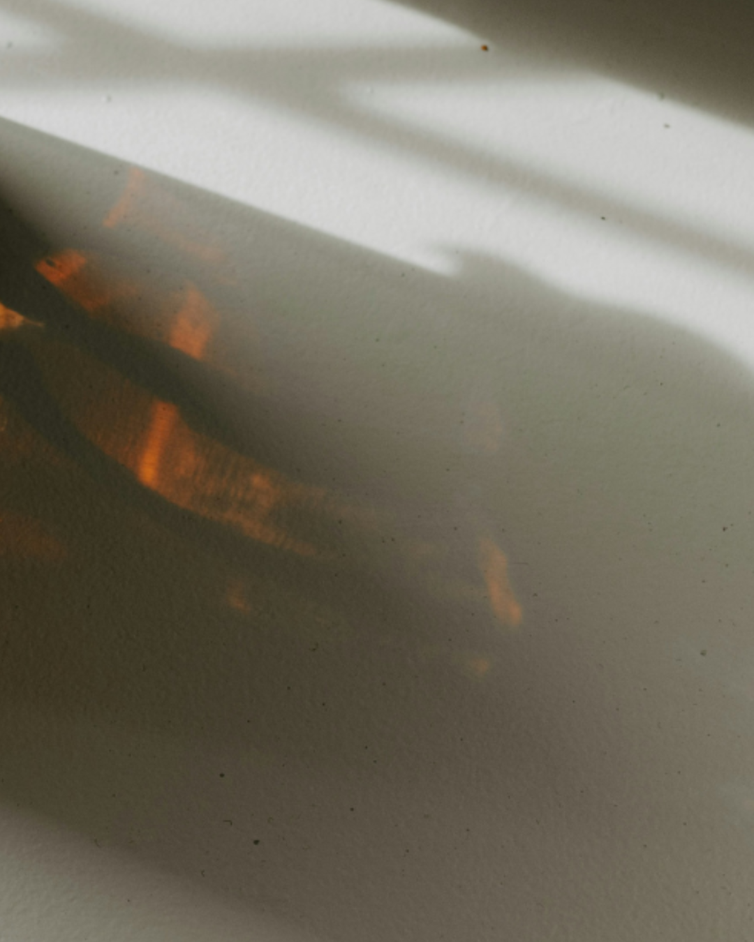 Shadow of an amber candle jar on a white surface.