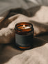 Frankincense + Myrrh Bare candle burning beside soft linen in warm atmospheric light.