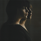 Two Gemini woman with emotionless expressions facing sideways on dark background.