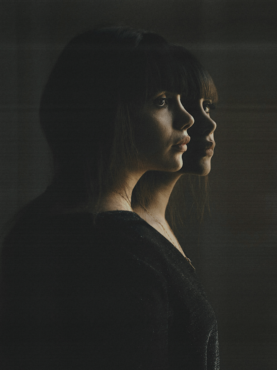 Two Gemini woman with emotionless expressions facing sideways on dark background.
